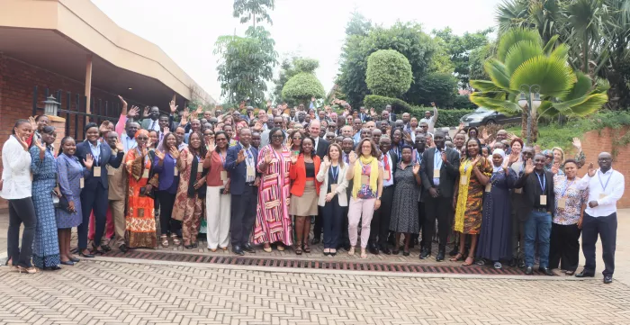Participants to the regional academy on fundamental principles and rights at work pose for a group photo, they are around 100 and some of them raise their hand in the photo