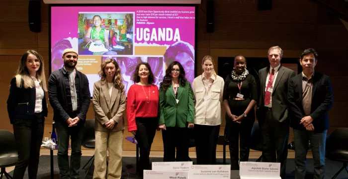 Nine individuals are side by side posing for a photo in front of a screen showing the name Uganda in a pink background