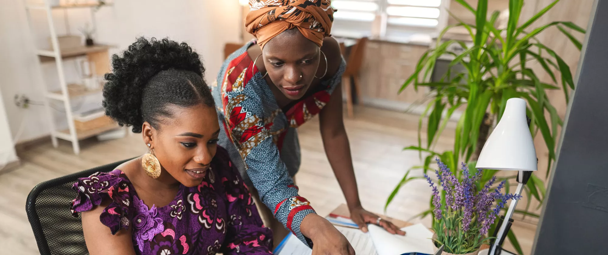 Two black female colleagues working together on laptop