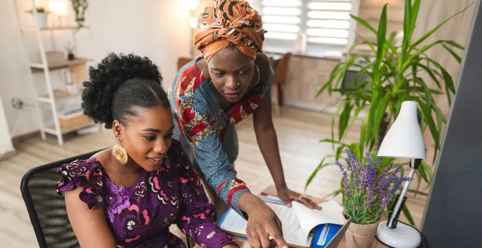 Two black female colleagues working together on laptop