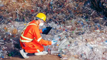 Worker at a recycling centre wearing a mask and helmet, holding an iPad